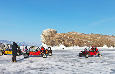 Frozen Lake Baikal on a sunny February day. A group of tourists travel on a buggy across the icy surface to the beautiful promontory of Ogoy Island. Winter unforgettable travel