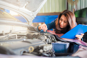 Wall Mural - Asian woman mechanic holding a clipboard of service order working  under the hood at the repair garage. Service and Maintenance car check. Copy space