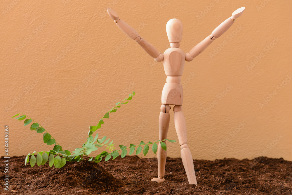 Wooden mannequin with plant and soil on color background