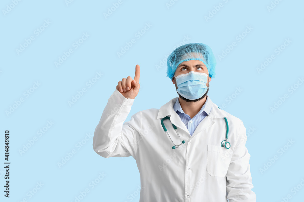 Doctor in medical mask pointing at something on color background