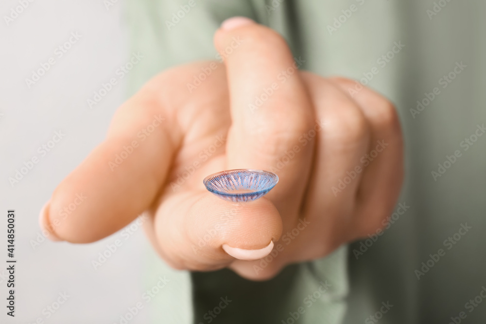 Female hand with contact lens on light background