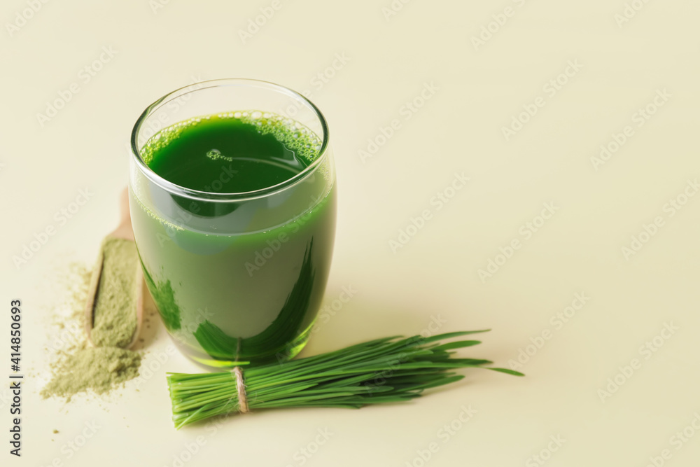 Glass with fresh wheatgrass juice and powder on light background