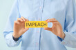 Woman holding paper with text IMPEACH on color background