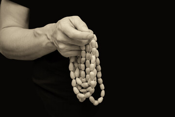 One man's hand touches a Buddhist rosary on a black, isolated background. Close-up, banner, copy space.