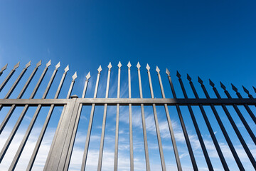 Closeup of a wrought iron gate with sharp points on blue sky with clouds and copy space.