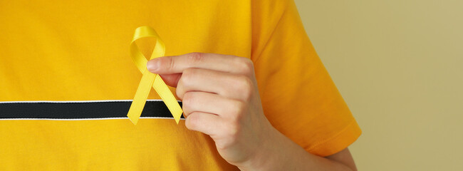 Woman in yellow t-shirt hold child cancer awareness ribbon