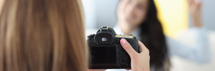 Black camera in hands of woman photographer with woman model on background in photo studio. Home photo session of friends tfc concept.