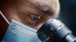 © Gorodenkoff - Ultra Macro Close Up Shot of a Male Scientist Wearing Surgical Mask and Looking into the Microscope. Microbiologist Working on Molecule Samples in Modern Laboratory with Technological Equipment.