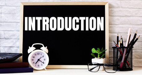 The word INTRODUCTION is written on the chalkboard next to the white alarm clock, glasses, potted plant, and pencils in a stand.