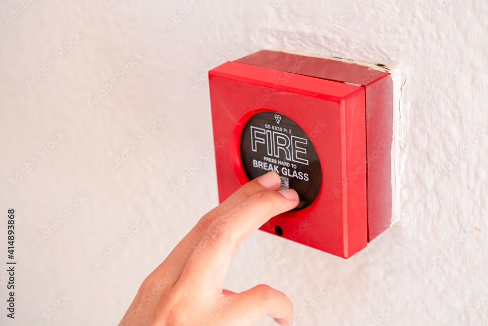 fingers pointing at old dirty red alarm on white rough concrete wall ...