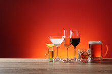 Different Alcohol Drinks On Wooden Table Against Red Background. Space For Text