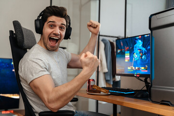 Wall Mural - Excited guy making winner gesture while playing video game on computer