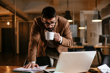 Wall Mural - Young businessman working on laptop and drinking coffee in his office. Businessman on coffee break.