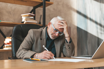A mature man is desperate to sign debt documents in the office at the table. Old man lost his job, stress and bankruptcy.