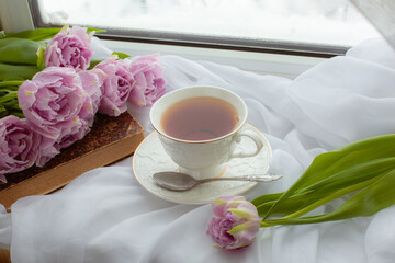 mug of tea an old book a bouquet of tulips on the window