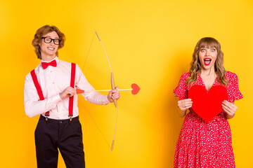 Sticker - Photo portrait of guy with arrow bow and amazed girl keeping red heart isolated on vibrant yellow background