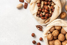 Walnuts, Peanuts, Hazelnuts, And Pecans In Shopping Bags On A White Background Top View. Copy Space For Text. Various Nuts.