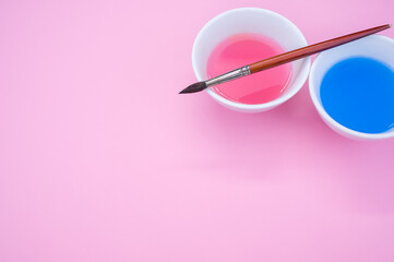 Wall Mural - High angle shot of pink and blue liquid watercolor paint on a bowl and paintbrush