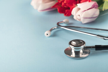 doctors day and world health day. medical stethoscope with bouquet of flowers on light blue backgrou