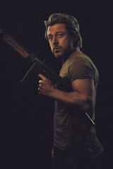 Rugged man with gun in green t-shirt against dark background.