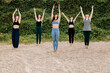 © Manu Reyes/Westend61 - Women and yoga instructor exercising with arms raised on sand against plants