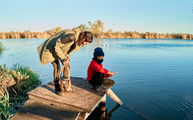 mother and her son in a red hat and shirt are playing with the lake water on the pier