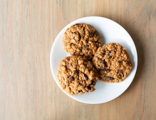 Wall Mural - Top view of homemade oatmeal raisin cookies on a white plate atop a table illuminated with natural light.