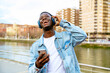 © Luis Manuel Munoz/ADDICTIVE STOCK - Young positive black male with cellphone listening to song from headphones while looking up on urban embankment