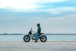 © Oscar Gimbal/ADDICTIVE STOCK - Side view of unrecognizable male biker in casual outfit and protective helmet sitting on motorcycle on embankment near sea at construction site