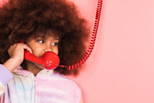 Ethnic Girl With Afro Hairstyle Talking On Old Fashioned Red Telephone In Studio And Looking Away On Pink Background