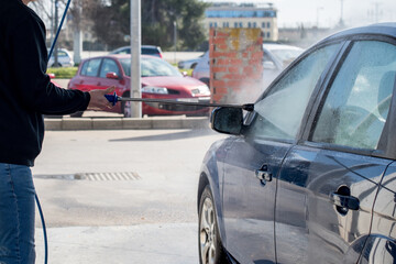 Lavado de coches. Hombre limpiando su coche con una manguera de agua a alta presión.