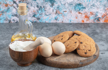 Oatmeal cookies with chocolate drops on a wooden board with ingredients around