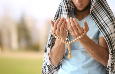 Young Muslim man praying on light background