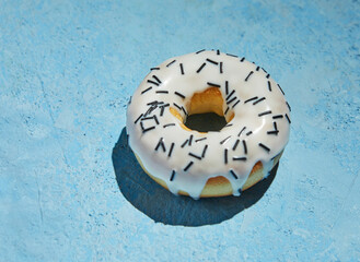 Donut with white frosting and sprinkles on blue background