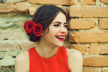 Smile teen of happy teenager girl smiling with dental braces on teeth, red lips, roses in brunette hair outdoors. Beauty salon.