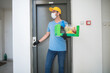 © astrosystem - Delivery guy in front of the building elevator with protective mask holding box with groceries and POS for contactless payment.