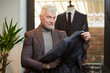 © Roman Tyukin - A mature man with gray hair and a sporty physique is checking a wool suit in a clothing store. A male customer with a beard in a boutique.
