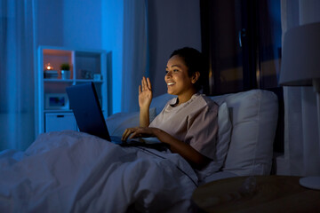 Sticker - technology, internet, communication and people concept - happy smiling young african american woman in glasses with laptop computer having video call in bed at home at night