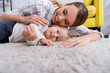 © LIGHTFIELD STUDIOS - surface level of happy mother with little son lying on carpet at home, blurred foreground