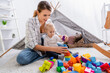 © LIGHTFIELD STUDIOS - young mother playing with construction blocks with son on floor near kids wigwam