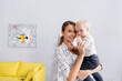 © LIGHTFIELD STUDIOS - happy woman smiling at camera while holding toddler son at home