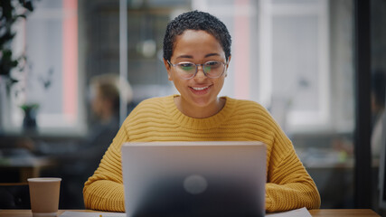 Wall Mural - Portrait of Young Latin Marketing Specialist in Glasses Working on Laptop Computer in Busy Creative Office Environment. Beautiful Diverse Multiethnic Female Project Manager is Browsing Internet.