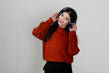 Pretty Young Girl Wearing Headphone And Listening To Music Or Songs With A Smile On Her Face, Raising Hands In Air, Standing Against White Backdrop.