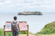 woman with backpack looking at information point by the sea coast
