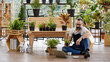 © Bangkok Click Studio - A beautiful bearded man sitting and using laptop notebook computer to sell plant in home indoor garden. Online marketing and live stream seller concept