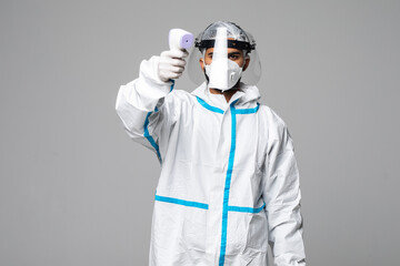 Wall Mural - Portrait of man medic wearing biological protective uniform suit clothing, mask, gloves measuring body temperature with infrared forehead thermometer gun on a white background