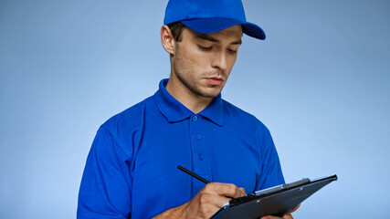 Wall Mural - young delivery man writing on clipboard isolated on blue