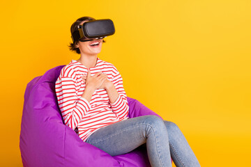 Poster - Photo of young beautiful pretty happy smiling cheerful girl in vr glasses sit armchair isolated on yellow color background