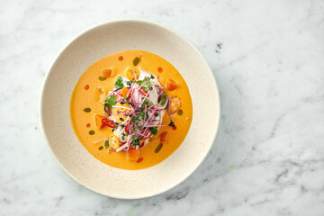 Peruvian cuisine dish - seabass ceviche with hot peppers, onions and yellow sauce, served in a white plate on a marble background. Restaurant seafood.