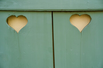 Green shutter with two hearts with yellow painted wall in the background.